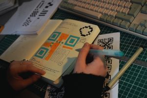 hands drawing a qr code in a notebook on a computer desk